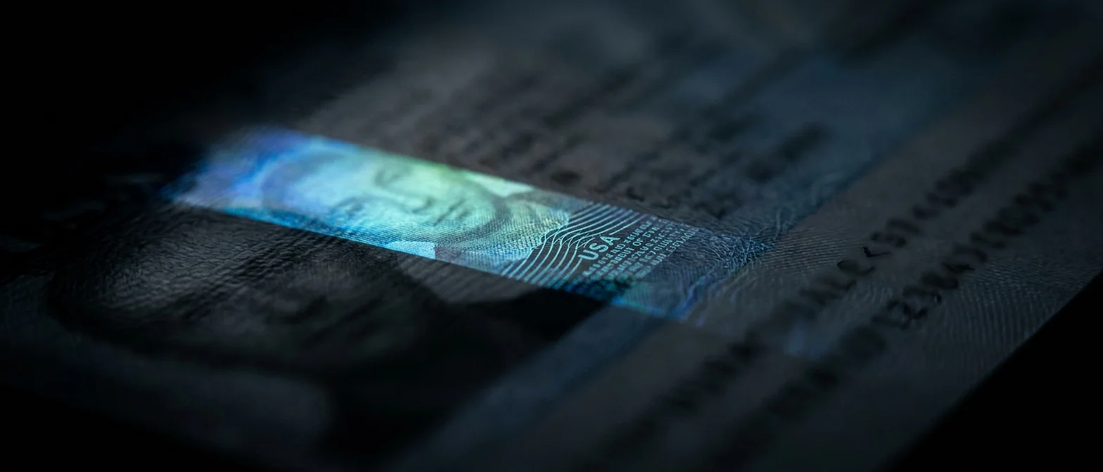 A narrow band of light across a US identity document, lighting its holographic security layer and the ghosted portrait inside it