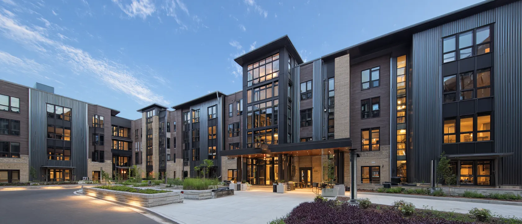 A large residential building at dusk, its windows and entrance lit under a deep blue sky